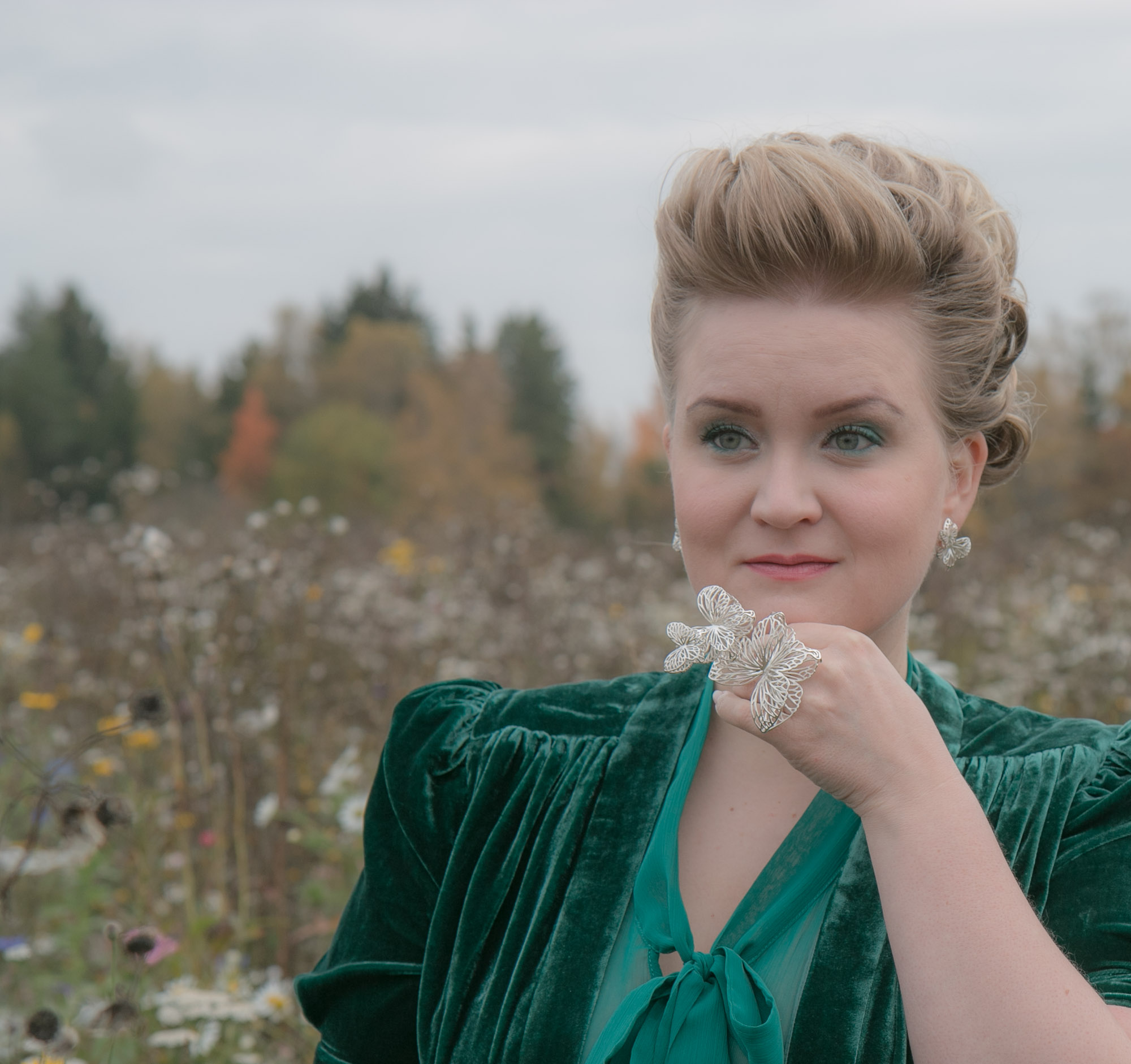 Iso perhosaiheinen statement-sormus ja vihreä iltapuku kukkaniityllä.